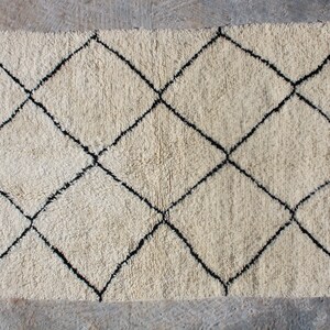 May include: A white rug with a black diamond pattern. The rug has a fringe border.