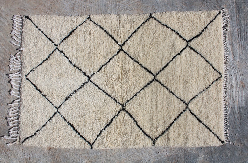 May include: A white rug with a black diamond pattern. The rug has a fringe border.