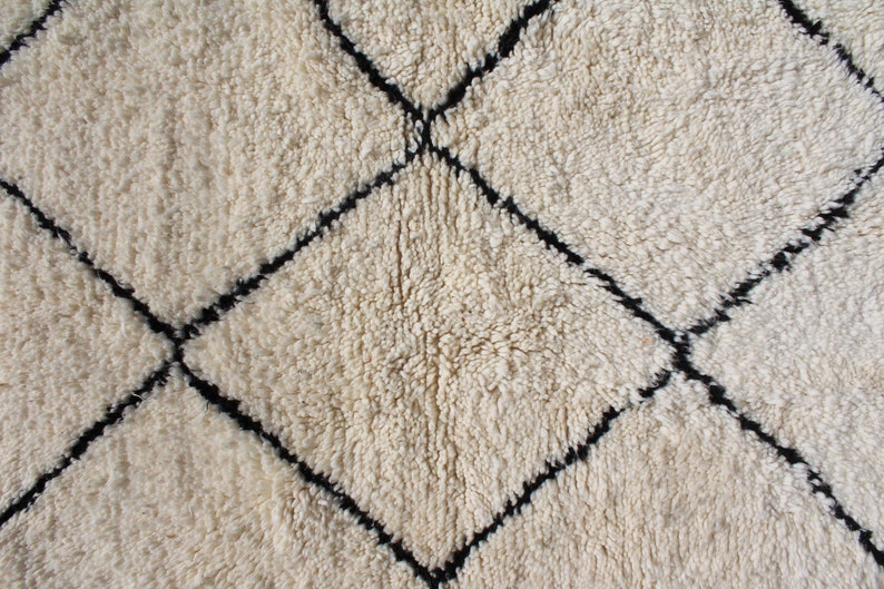 May include: A white rug with a black diamond pattern. The rug is made of a soft, fluffy material.