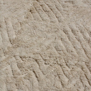 Puede incluir: Primer plano de una alfombra de color crema con un patr&oacute;n de rombos tejido. La alfombra tiene una textura suave y esponjosa.