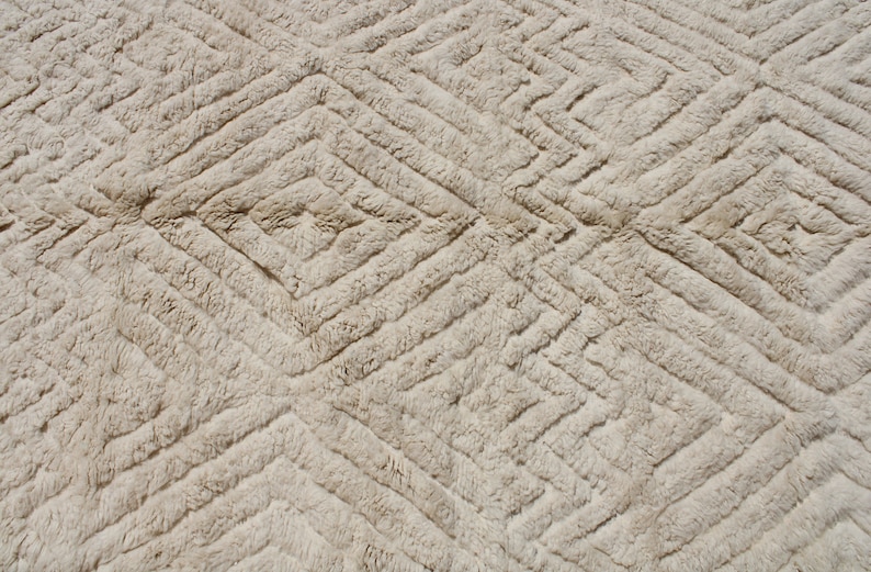 Puede incluir: Primer plano de una alfombra beige con un patr&oacute;n de diamantes. La alfombra est&aacute; hecha de un material suave y esponjoso.
