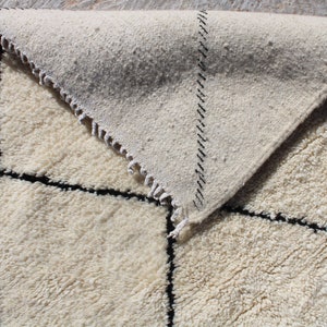 May include: A white and black Moroccan rug with a geometric pattern. The rug is made of wool and has a soft, fluffy texture.