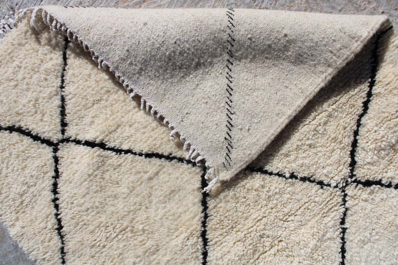 May include: A white and black Moroccan rug with a geometric pattern. The rug is made of wool and has a soft, fluffy texture.