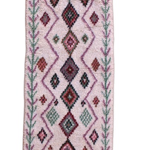 May include: A long, rectangular rug with a pink background and a geometric pattern in shades of green, red, and purple. The rug has fringe on all four sides.