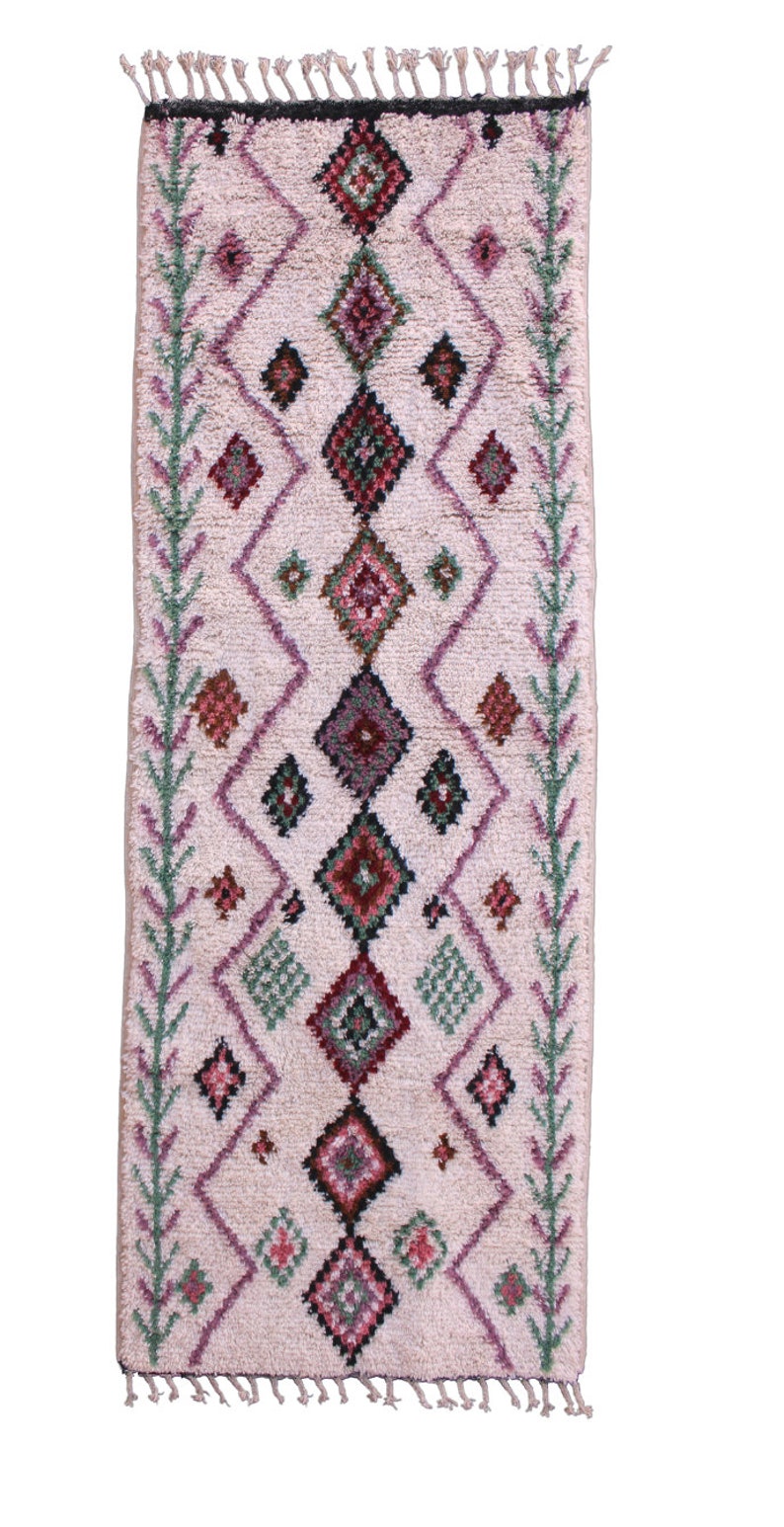 May include: A long, rectangular rug with a pink background and a geometric pattern in shades of green, red, and purple. The rug has fringe on all four sides.