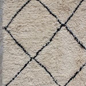 May include: A white Moroccan rug with a black diamond pattern. The rug has a fringe border.