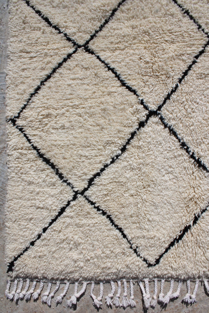 May include: A white Moroccan rug with a black diamond pattern. The rug has a fringe border.
