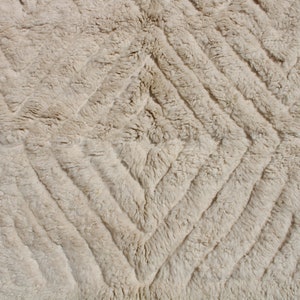 Puede incluir: Primer plano de una alfombra beige con un patr&oacute;n de diamantes. La alfombra est&aacute; hecha de un material suave y esponjoso.