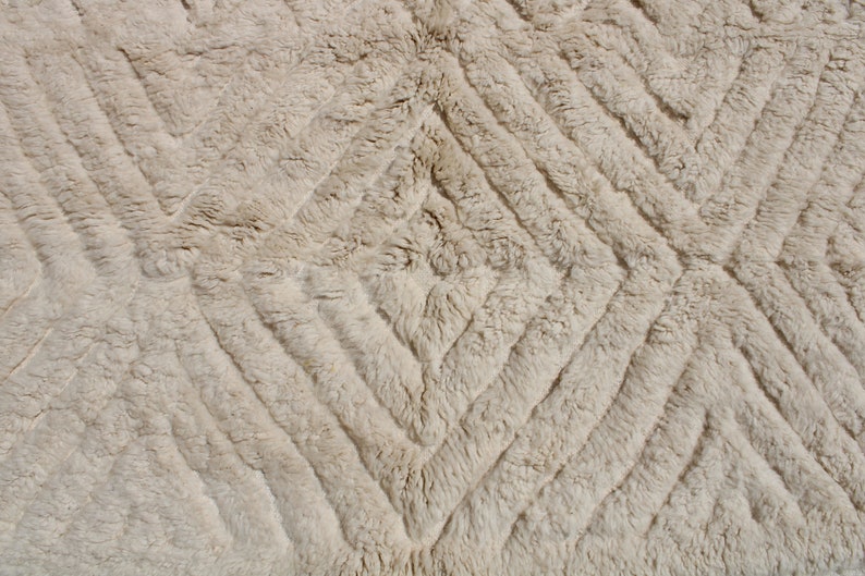 Puede incluir: Primer plano de una alfombra beige con un patr&oacute;n de diamantes. La alfombra est&aacute; hecha de un material suave y esponjoso.