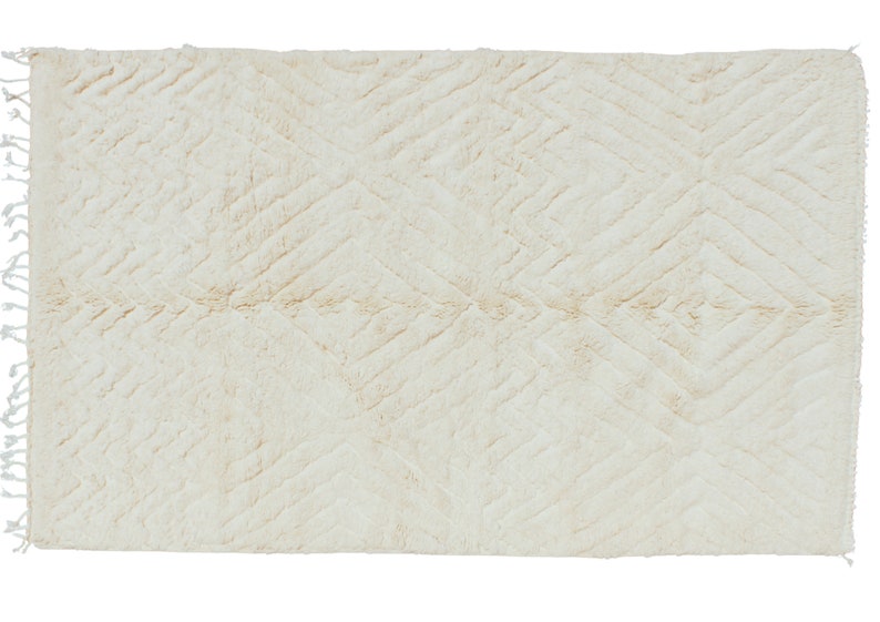 Puede incluir: Una alfombra blanca y esponjosa con un patr&oacute;n de diamantes tejido en la tela. La alfombra tiene un borde de flecos.