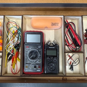 May include: A wooden drawer organizer filled with various electronic tools and accessories. Includes a multimeter, a Tascam recorder, an orange Stanton Optical case, screwdrivers, and test leads. The drawer is divided into compartments.