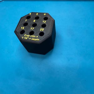 May include: Black hexagonal tool holder with numbered holes. The text "Cup size & 1.16" a depth" is printed in yellow. The holder is on a blue surface.
