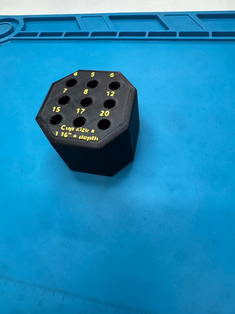 May include: Black hexagonal tool holder with numbered holes. The text "Cup size & 1.16" a depth" is printed in yellow. The holder is on a blue surface.