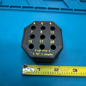 May include: Black, octagonal tool holder with numbered holes. Numbers 4, 5, 6, 7, 8, 12, 15, 17, and 20 are visible. Text reads "Cup size & 1.16" depth." A yellow tape measure is next to the tool holder.