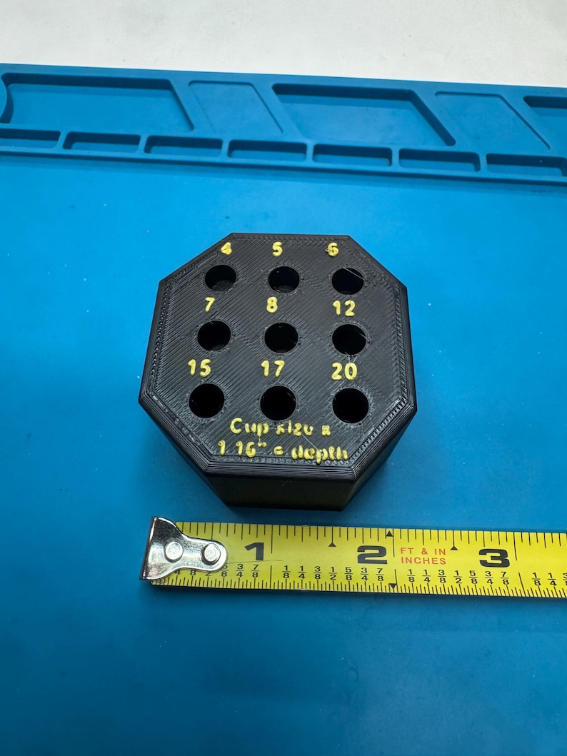 May include: Black, octagonal tool holder with numbered holes. Numbers 4, 5, 6, 7, 8, 12, 15, 17, and 20 are visible. Text reads "Cup size & 1.16" depth." A yellow tape measure is next to the tool holder.
