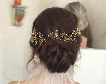 May include: A white bridal veil with a delicate tulle fabric. The veil is worn over a white tank top and a dark green skirt. The bride's hair is styled in a low bun with a gold and pearl hairpiece.