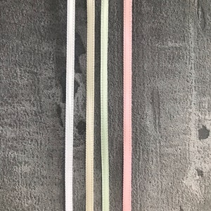 May include: Five different colored satin ribbons on a gray textured background. The ribbons are white, cream, light green, and pink.