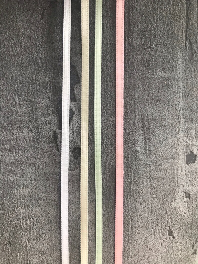 May include: Five different colored satin ribbons on a gray textured background. The ribbons are white, cream, light green, and pink.