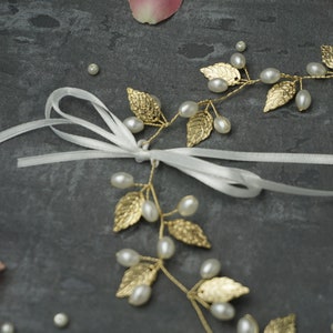 May include: A gold leaf and pearl hair vine with a white satin ribbon. The vine is made of delicate gold leaves and pearls, and the ribbon is tied in a bow.