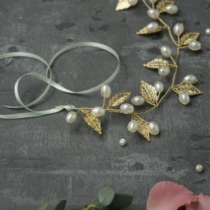 May include: A gold leaf and pearl hair vine with a light green ribbon. The vine is made of gold wire with small gold leaves and white pearls. The ribbon is tied in a bow.