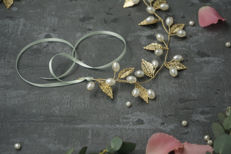 May include: A gold leaf and pearl hair vine with a light green ribbon. The vine is made of gold wire with small gold leaves and white pearls. The ribbon is tied in a bow.