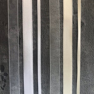 May include: Assortment of white and ivory ribbon trims, including sheer and satin, displayed against a dark gray background.