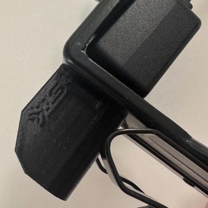May include: A black plastic wall mount with a metal clamp and a black power adapter attached. The mount has the text "X-SIGHT" printed on it.