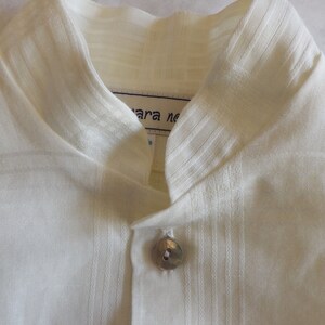 May include: White linen shirt with a mandarin collar and a single button closure. The shirt has a textured weave and a label that reads "Mara ne".