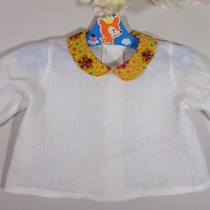 May include: White long-sleeved shirt with a yellow and floral patterned collar. The shirt is hanging on a blue hanger with a cartoon fox design. The shirt is made of a lightweight fabric.