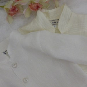 May include: Two white linen shirts with button closures. The shirt on top has a collar and a label that reads "cara ma".