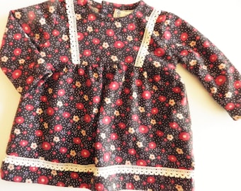May include: A dark brown long-sleeved dress with a floral print and white lace trim. The dress has a round neckline and a gathered skirt.