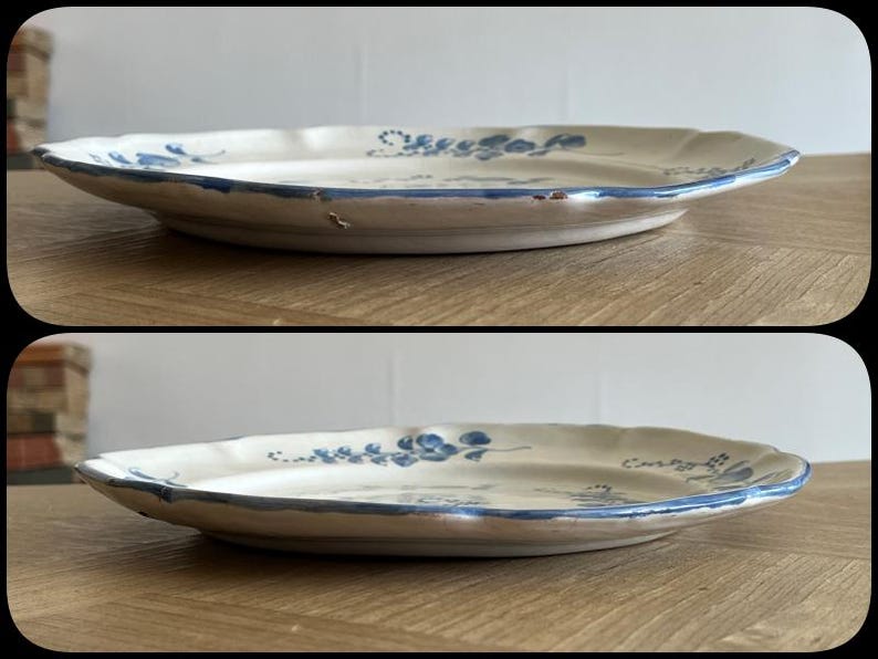 May include: A round ceramic plate with a cream-colored base and a scalloped edge. The plate features hand-painted blue floral motifs and a thin blue line along the rim. The surface shows visible signs of wear and minor chipping along the edge.