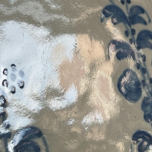 May include: A glazed ceramic surface with a light tan base color featuring hand-painted dark blue floral motifs. The design includes clusters of small circular dots and stylized leaf patterns arranged in a vertical vine-like formation on the right.