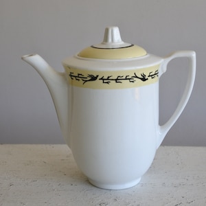 Peut inclure: Cafetière en céramique blanche avec un motif floral jaune et noir autour du haut.