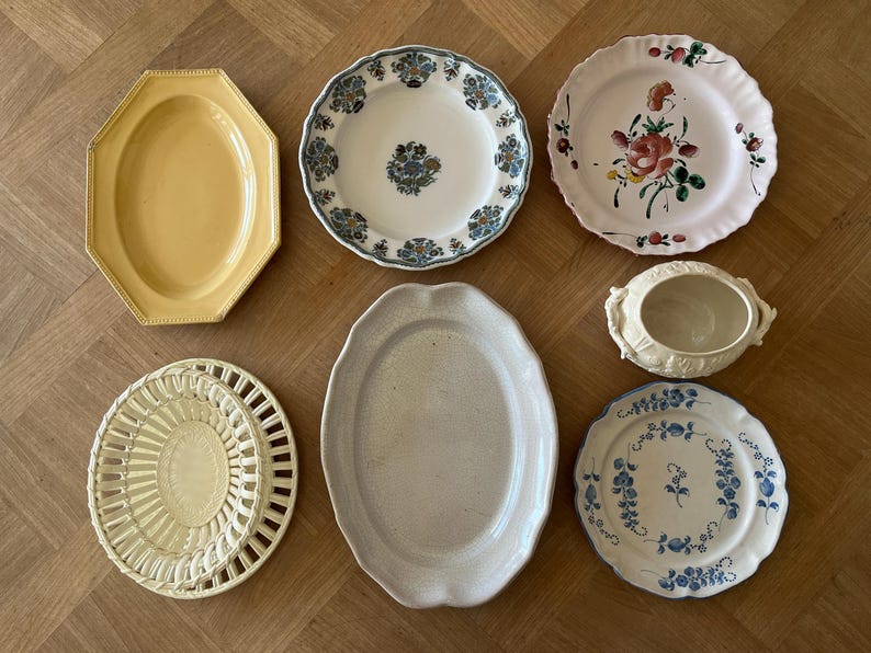 May include: A collection of seven ceramic pieces including a yellow octagonal platter, a white plate with blue floral patterns, a white plate with a pink rose motif, a cream lidded tureen, a cream lattice-rimmed plate, a plain oval platter, and a blue floral plate.