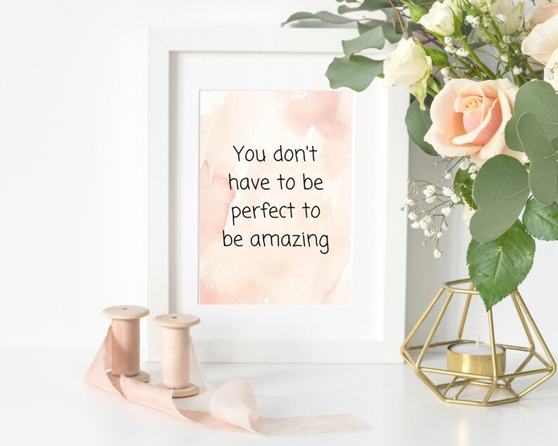 Peut inclure: Impression encadr&eacute;e blanche avec un fond aquarelle et le texte "You don't have to be perfect to be amazing". L'impression est pos&eacute;e sur une surface blanche avec un bougeoir en m&eacute;tal dor&eacute; et deux bobines de ruban rose.