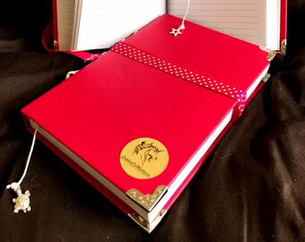 May include: Red journal with lined pages, a white ribbon bookmark, and gold-colored corner protectors. The journal has a gold emblem with a unicorn design and the text "Leather Collections". A second journal is open in the background.