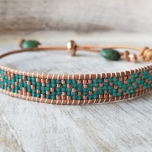 Puede incluir: Un brazalete de cuentas turquesa y cobre con un cordón de cuero marrón y un cierre de nudo deslizante.