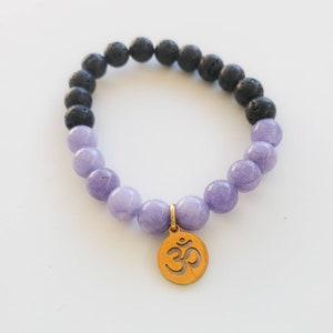 May include: A purple and black beaded bracelet with an Om charm. The bracelet is made with lava rock and amethyst beads.