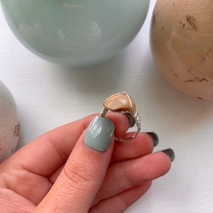 K&ouml;nnte beinhalten: Ein Ring aus silbernem Draht mit einem hellbraunen Stein. Der Ring wird von einer Hand mit hellgr&uuml;nem Nagellack gehalten.