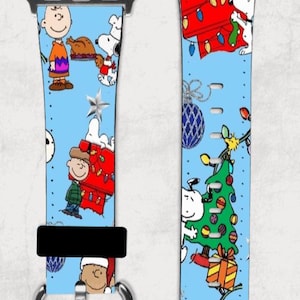 Puede incluir: Una banda azul para Apple Watch con un diseño navideño con Snoopy y Charlie Brown. La banda tiene un fondo blanco con acentos rojos y verdes. El diseño incluye un árbol de Navidad, una casa y un pavo.