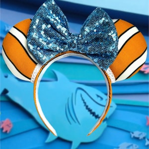 May include: A themed headband featuring orange and white striped ears, a large blue sequined bow, and a white headband. The design is inspired by a popular animated film, perfect for theme park visits or cosplay.