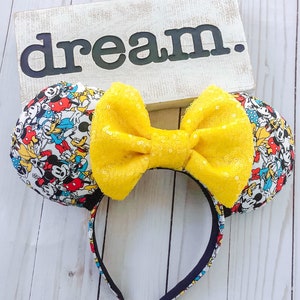 May include: Mickey Mouse and friends character print Minnie Mouse ears headband with a large yellow bow. The headband is black and the bow is made of sequins.