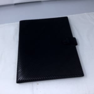 May include: A black leather folder with a textured surface and a metal clasp.