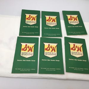 May include: Six green and yellow S&H Green Stamps booklets. Each booklet has the text "S&H Green Stamps" and "America's Most Valuable Stamps" printed on the front. The text "The Sperry and Hutchinson Company Established 1896" is printed on the bottom of each booklet.