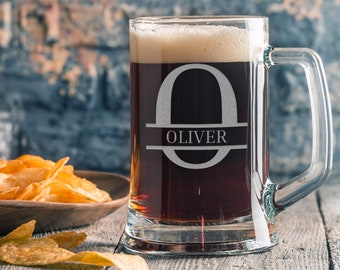 May include: A clear glass beer mug with a handle, filled with dark beer and a white foam head. The mug is etched with a large letter "O" and the name "OLIVER" below it.