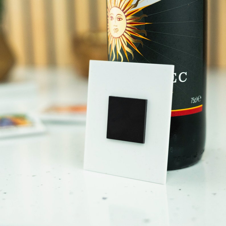 May include: A white square magnet with a black square in the center. The magnet is attached to a white surface. The text "EC" is visible on the right side of the image.