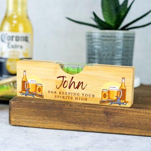 K&ouml;nnte beinhalten: Ein personalisiertes Bambus-Wasserwaage mit einer gr&uuml;nen Libelle und einem Bier-Design. Die Wasserwaage lautet "John for keeping your spirits high".