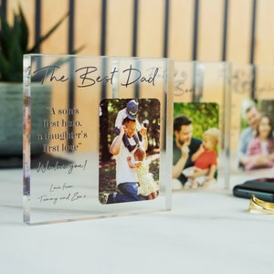 Może przedstawiać: Przezroczysty akrylowy blok fotograficzny z napisem "The Best Dad" i zdjęciem rodzinnym. Blok zawiera cytat "A son's first hero, a daughter's first love." i wiadomość "We love you!" z osobistym podpisem.