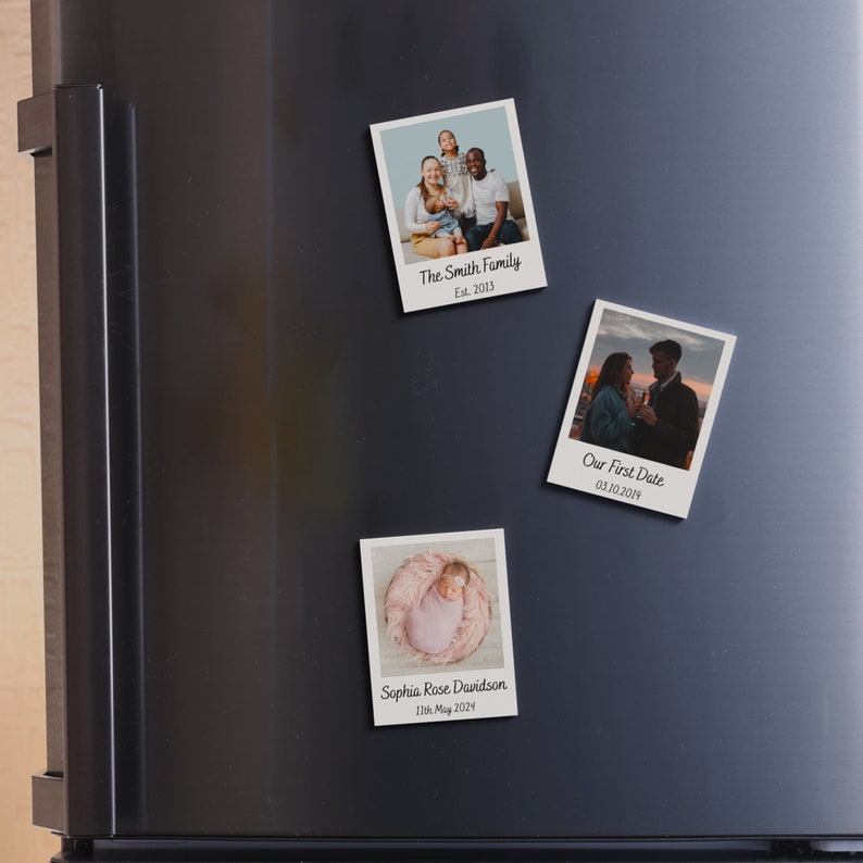 May include: Three Polaroid-style photo magnets with white borders and black text. The top magnet shows a family of four, the middle magnet shows a couple, and the bottom magnet shows a baby. The text on the magnets reads "The Smith Family Est. 2013", "Our First Date 03.10.2014", and "Sophia Rose Davidson 11th May 2024".